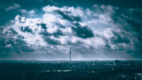 Blick über eine Stadtlandschaft mit Wolken und einem hohen Fernsehturm.