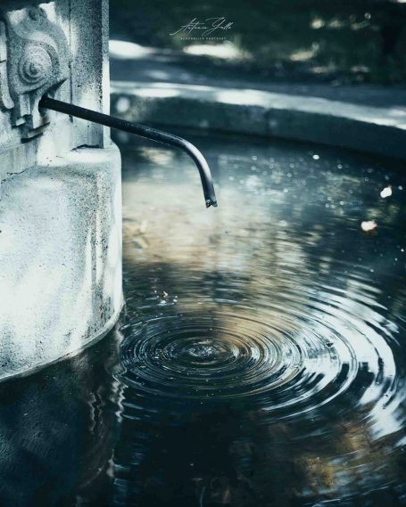 Ein Wasserhahn mit fließendem Wasser, das Wellen im ruhigen Wasser erzeugt.