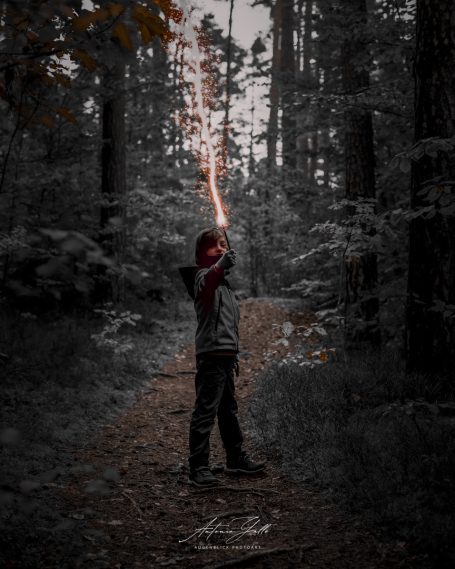 Junge steht im Wald und hält einen leuchtenden Zauberstab hoch.