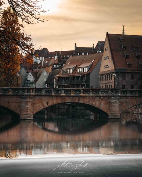 Spiegelung von alten Häusern an einer Brücke mit sanftem Sonnenlicht.