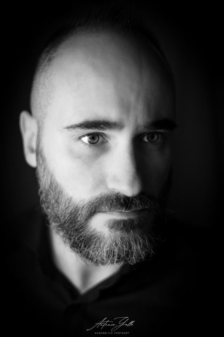 Porträt eines Mannes mit glattem Kopf und Bart, ernstes Gesicht in Schwarz-Weiß.