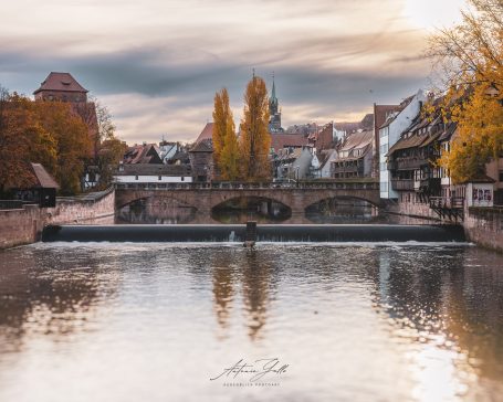 Herbstliche Stadtansicht mit Brücke und ruhigem Wasser, reflektierenden Bäumen.